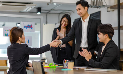 Closeup shot of handshaking of unrecognizable unknown male businessman and female businesswoman in meeting room after business agreement deal done while colleagues clapping hands celebrating together