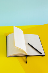Open blank notebook and black pencil on yellow and blue background