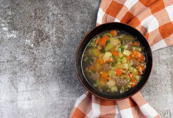 Meatball soup with vegetables and herbs in a bowl on a dark background. Top view, flat lay