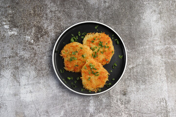 Rustic hash browns with chives on a round plate on a dark background. Top view, flat lay
