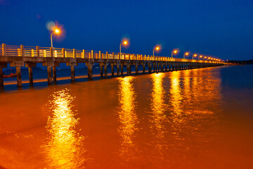 Fototapeta premium Pier at night with yellow lights on a background of blue sky