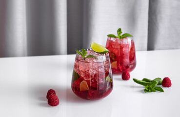 Fresh summer lemonade with raspberry, lime, soda water, and ice in glasses. Cold refreshing drink, cocktail or mocktail.