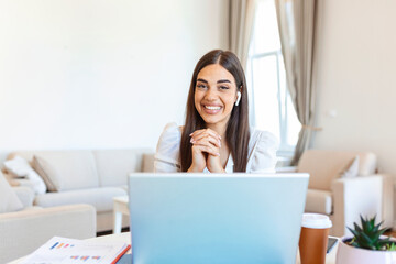 Excited young woman looking at camera, holding funny conversation with colleagues online, webcam view. Head shot of young woman with headphones laughing, having fun from home office.