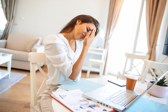 Young frustrated woman working from home office in front of laptop suffering from chronic daily headaches, treatment online, appointing to a medical consultation, electromagnetic radiation, sick pay