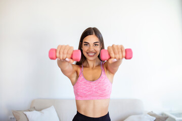 Woman exercising with dumbbells at home. Sporty beautiful woman exercising at home to stay fit. Young woman exercising at home in a living room. Fitness, workout, healthy living and diet concept.