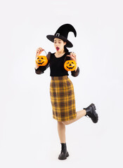 Halloween theme, pretty asian girl in black long sleeve t-shirt and yellow striped skirt wear witch hat holding orange pumpkin lantern and bucket on whtie background.