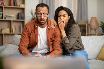Shocked African American Couple Watching Shocking TV Content At Home