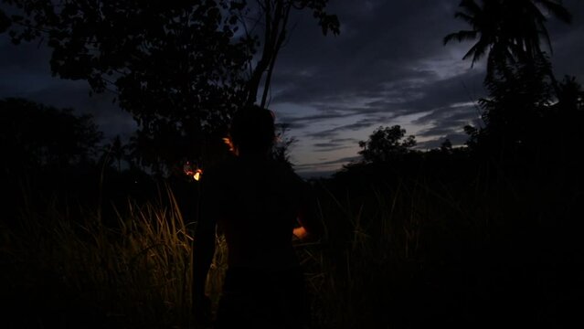 Scared man walks in a jungle surrounded by tall grass and waves a burning torch for protection. View behind the back