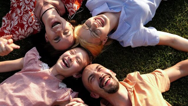 A happy family with children lying on the grass in a circle and laughing.