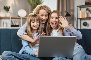 Single Caucasian mother and little children sitting on couch using laptop, family enjoy distant talk by video call, spend time in internet buying, e-commerce users, cartoons or video fun concept