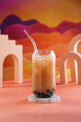 One glass with trendy asian drink iced boba bubble tea with tapioca pearls and milk with glass drinking straw on bright colorful red and orange background