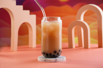 One glass with trendy asian drink iced boba bubble tea with tapioca pearls and milk with glass drinking straw on bright colorful red and orange background