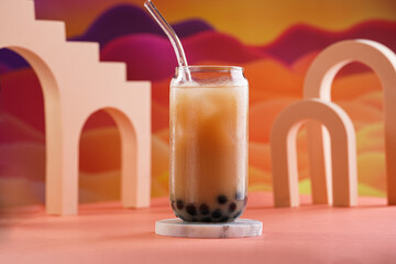 One glass with trendy asian drink iced boba bubble tea with tapioca pearls and milk with glass drinking straw on bright colorful red and orange background