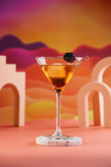 One martini glass with ice cube and brown alcoholic drink with black berry on bright colorful red and orange background