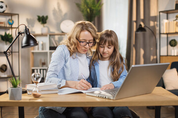 Caucasian tutor engaged with schoolgirl help complete tasks sitting at table at home. Concept of education child development, little child homeschooling writing homework with stepmother.