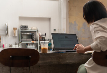 Soft focus, Young Asian woman sitting alone at a counter in a cafe working on a laptop