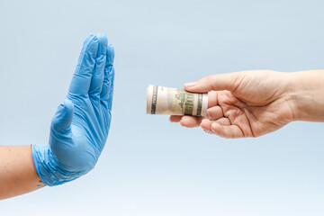 Naklejka premium Offering money (dollars) to a hand in blue surgical glove, nurse or doctor. Corruption.