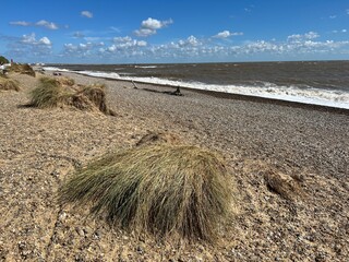 Landscape view of beautiful Walberswick beach East Anglia Suffolk uk with sea waves pebble sand shore with natural grassy banks and blue sky with white cloud on Summer holiday day light