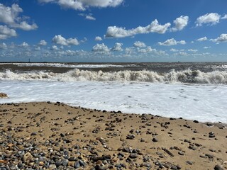Landscape view of beautiful Walberswick beach East Anglia Suffolk uk with sea waves pebble sand shore with natural grassy banks and blue sky with white cloud on Summer holiday day light