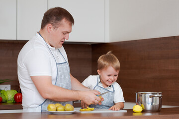 Concept food and nutrition. Shot of two cheerful dad and son posing in kitchen peeling potatoes...