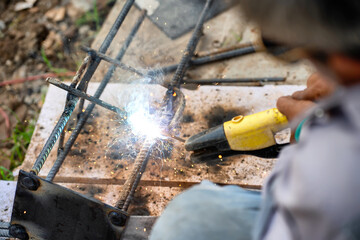 Asian welders use electric welding tools to install columnar foundation in construction site.