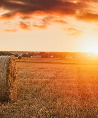 Printed roller blinds orange glow Dramatic beautiful landscape of a harvested field with a hay bale roll. Summer sunset in the rural area. Warm countryside harvesting meadow panorama.