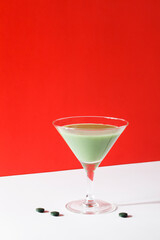 green smoothie in martini cocktail glass with spirulina algae pills on red background. self care and minimal healthy party life concept. copy space