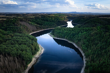 Obraz na płótnie Canvas Aerial view of a blue river in a dam and a lush green forest, mountains in the background, in Germany, Europe