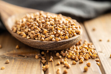 Uncooked buckwheat grain in wooden spoon on wooden table.