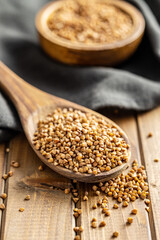 Uncooked buckwheat grain in wooden spoon on wooden table.