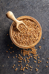 Uncooked buckwheat grain in bowl on black table. Top view.