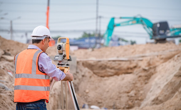 Surveyor engineer wearing safety uniform ,helmet and radio communication with equipment theodolite to measurement positioning on the construction site of the road with construct machinery background