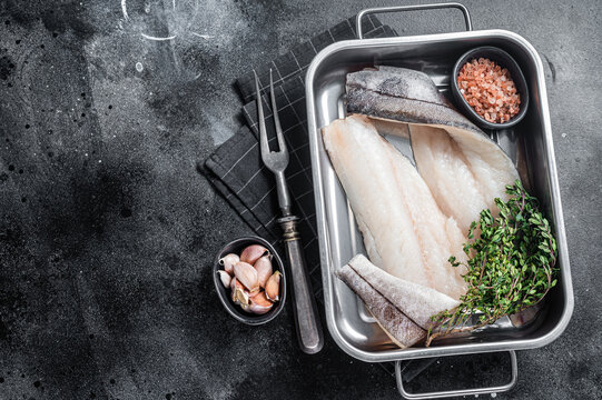 Raw haddock fish fillets, whitefish meat in kitchen tray with thyme. Black background. Top view. Copy space