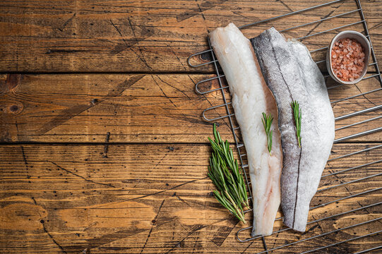 Raw fish fillets on grill with rosemary and herbs. Wooden background. Top view. Copy space