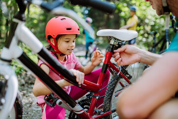 Young family with little children preapring for bike ride, standing with bicycles in nature.