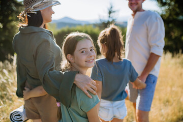 Happy young parents with daughters walking for picnic in nature in summer day,