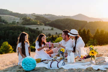 Happy family with children having picnic in nature, giving each other gifts.