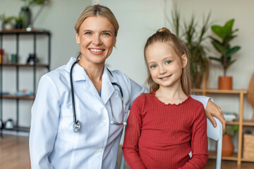 Obraz premium Portrait of happy pediatrician and pretty child girl looking and smiling at camera, sitting in doctor's office