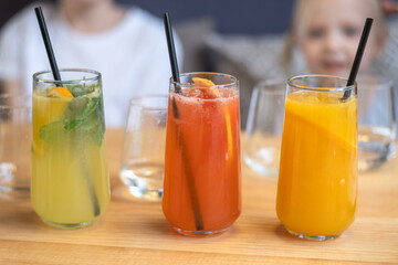 Bright colorful drinks, fresh lemonade.. Glasses with fruit juices and lemonade in front of children.