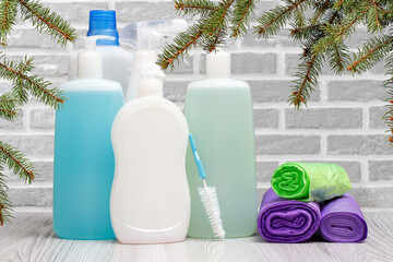 Bottles of dishwashing liquid, brushes and garbage bags with gray wall on background.