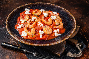 Saganaki Shrimp prawns with tomato and feta cheese on a plate. Dark background. Top view.