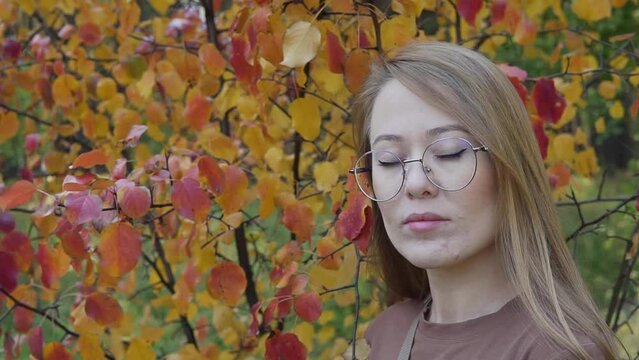 Woman feeling autumn weather in the forest park at sunset. Fall season yellow foliage starts. Moody day woods holiday journey. The face of a thoughtful girl with glasses in autumn outdoors travel.