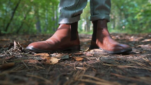 Hiking in a park. Feet in brown chelsea boots walking on forest path. Girl feet tracking on sunny day outdoors.
