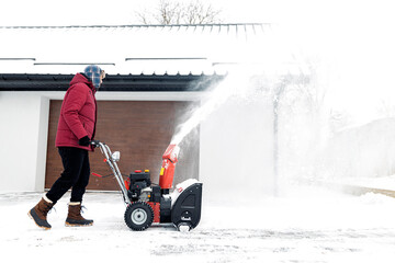 Snow blower powered by gasoline in action. Man outdoor in front of house using snowblower machine....