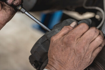 A mechanic pries off the brake caliper off of the brake pads with a screwdriver. Old brake pad...
