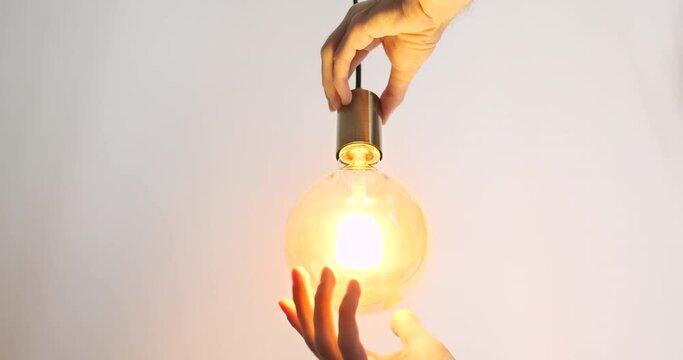 Male hands screw a light bulb into a socket. Close-up. Yellow bright light, the light bulb on the wire lights up.