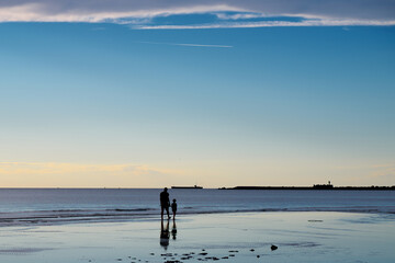 Fototapeta na wymiar Father and son walk along the seashore at sunset. Silhouettes of two people. The ebb of the sea.