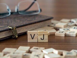 vj word or concept represented by wooden letter tiles on a wooden table with glasses and a book