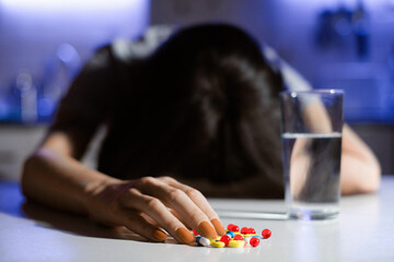 An unrecognizable woman is lying face down on a table in depression or headache. Selective focus on the pill hand. - 528884998