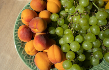 Pile of small peaches or peach plums and bunch of green grapes on a plate.